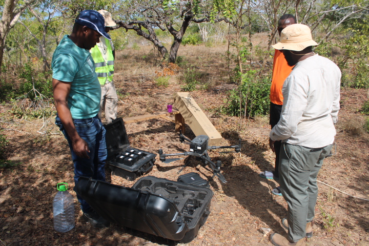 Four archaeologists stand around a drone, preparing it for take-off.